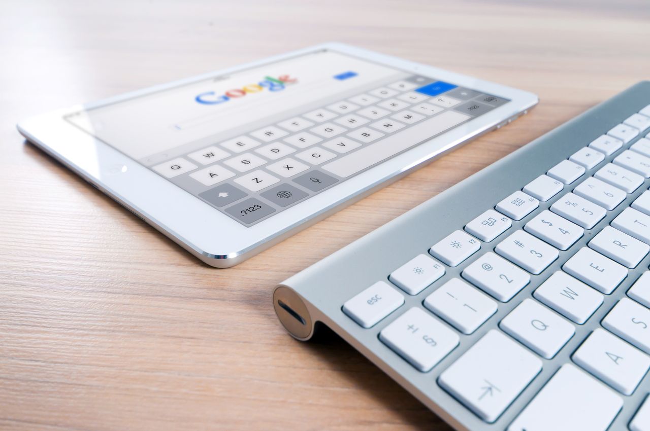 services-04 A modern tablet displaying a search engine logo next to a wireless keyboard on a wooden desk.